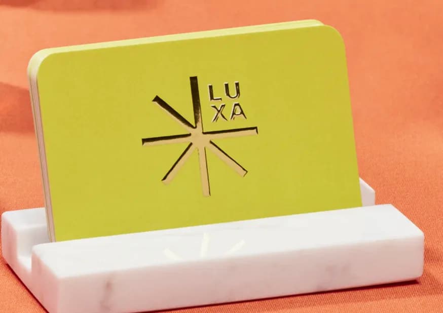 A lime green card with the LUXA logo pressed into it, standing in a marble holder.